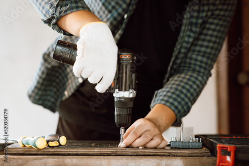 Close up of male mechanic holding electric cordless screwdriver drill with wood screw in the factory. Working with the screw. Professional carpenter. Concept furniture at home.