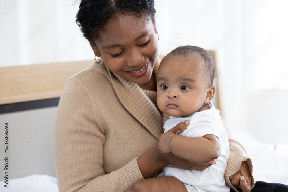 close up African young mother carrying and playing with her adorable baby on bed close up African young mother carrying and playing with her adorable baby on bed
