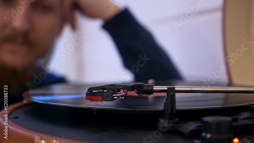 Close-up of a man putting a vinyl record into a turntable, the record starts spinning and a needle is slowly lowered onto it to play music. Vintage listening to music at home.