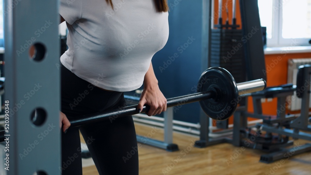 A young woman is engaged in a fitness club according to an individual program. A woman performs a straight-grip barbell row. Exercise is used to develop the back muscles. Woman doing sports exercises. A young woman is engaged in a fitness club according to an individual program. A woman performs a straight-grip barbell row. Exercise is used to develop the back muscles. Woman doing sports exercises.
