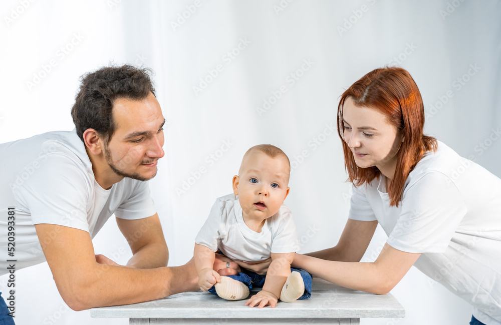 young parents lovingly look, play, kiss the child. white interior young parents lovingly look, play, kiss the child. white interior