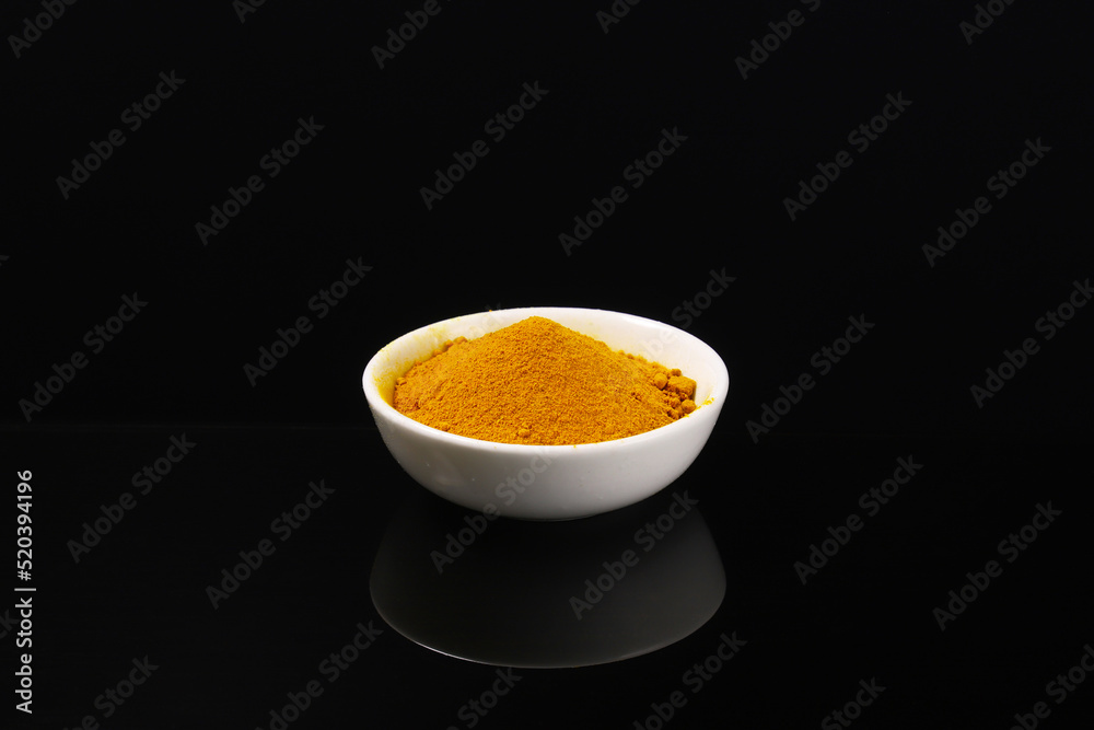 Ground turmeric in a white plate on a dark table with reflection. Close-up Ground turmeric in a white plate on a dark table with reflection. Close-up