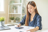 Account finance, asian young business woman hand use calculator for calculate budget, cost and income of company from bills, reports paperwork, plan spend money expenses, working on desk at home.