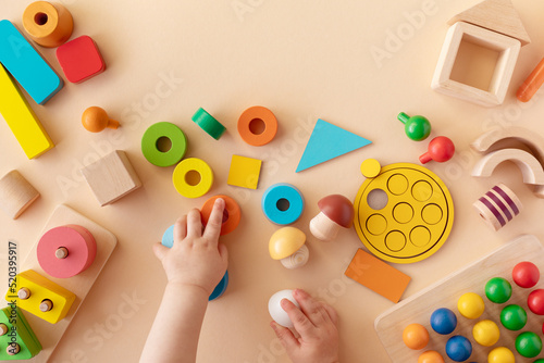 Toddler activity for motor and sensory development. Baby hands with colorful wooden toys on table from above.