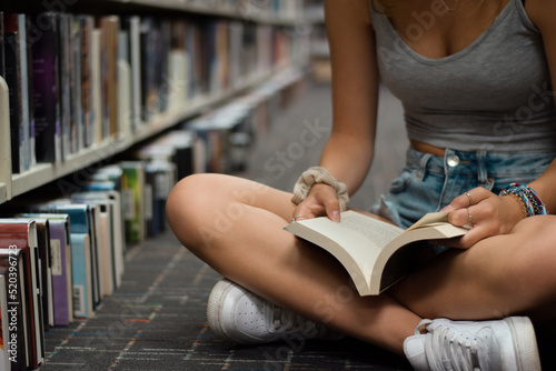 Young girl sitting on floor at library reading book
