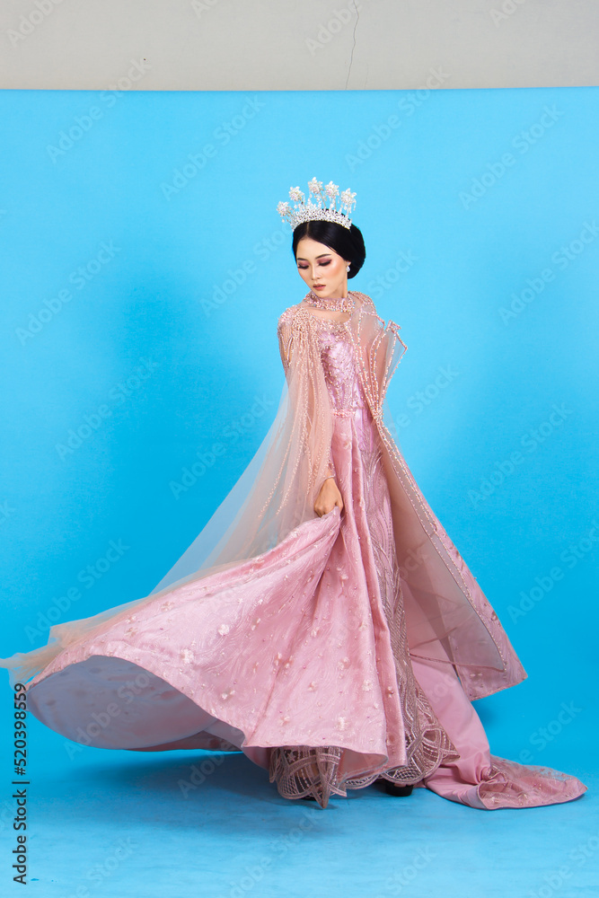 Obraz premium Portrait of asian woman in beautiful makeup wearing pink wedding dress, isolated on blue background.