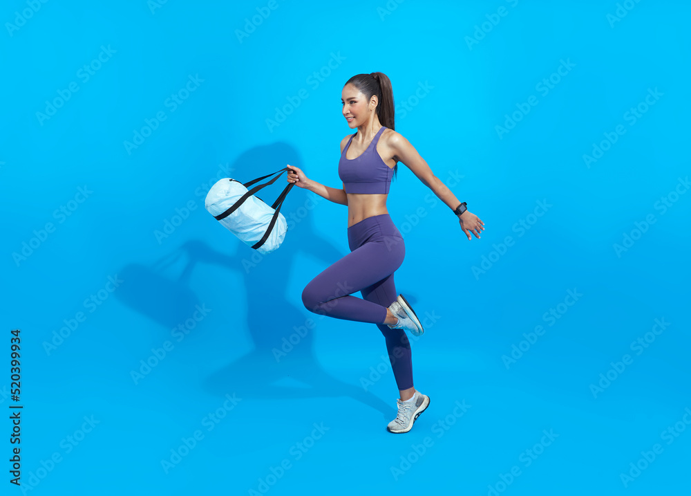 Go to training fitness. Happy Asian sporty woman with bag running on blue background. Sports and healthy lifestyle