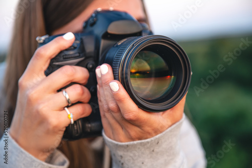 A young woman with a professional camera takes a photo in nature.