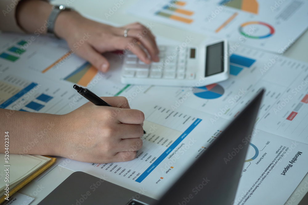 Closeup Portrait of a female accountant using a calculator and laptop to calculate balance using graphs for customers. Closeup Portrait of a female accountant using a calculator and laptop to calculate balance using graphs for customers.