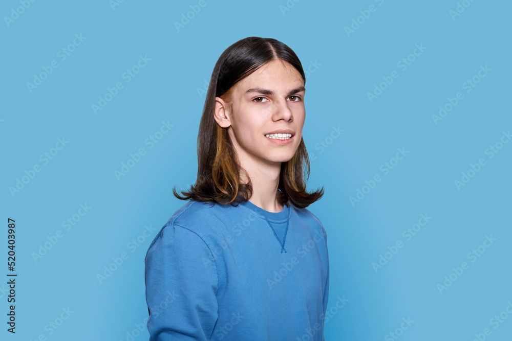 Headshot portrait of teenage guy looking at camera on blue background Headshot portrait of teenage guy looking at camera on blue background