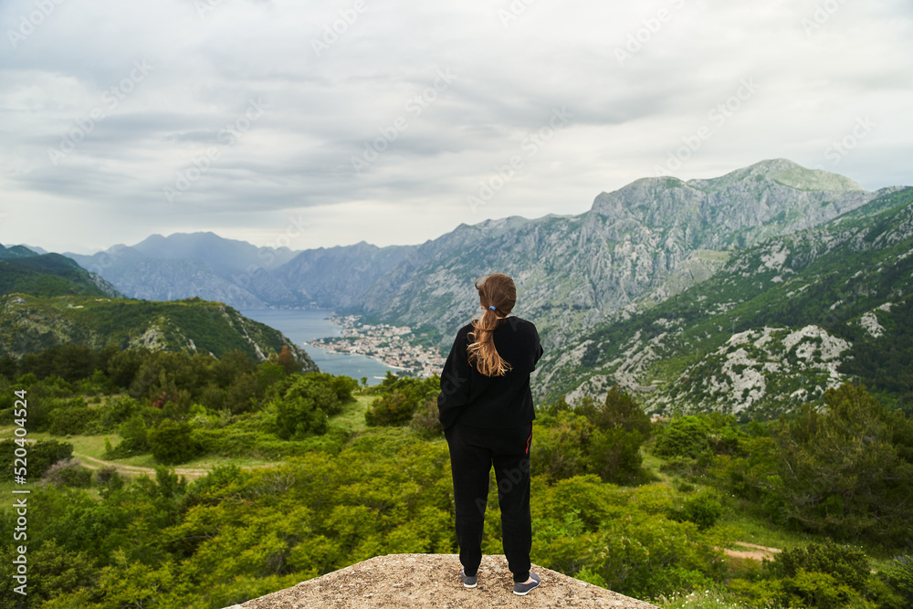 Kotor, Montenegro - May 30, 2021: View of the back of a girl in a black tracksuit looking at Kotor and Koto-Bay bay