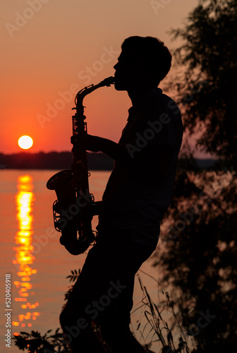 Silhouette of a young guy playing the saxophone in the evening at sunset