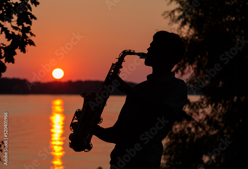 Silhouette of a young guy playing the saxophone in the evening at sunset
