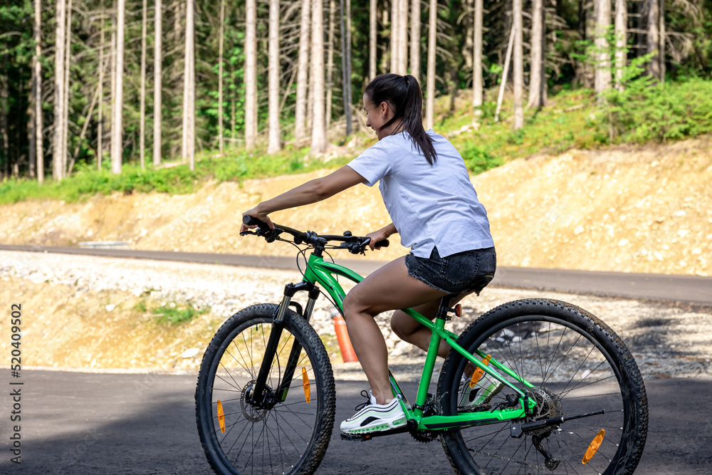 A young woman rides a bicycle in a mountainous area in the forest.