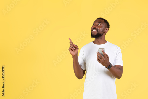 African Man Holding Phone Pointing Fingers Aside On Yellow Background