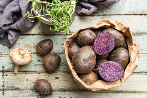 Close up of farm fresh purple potatoes in a paper bag on white wooden background, top view photo