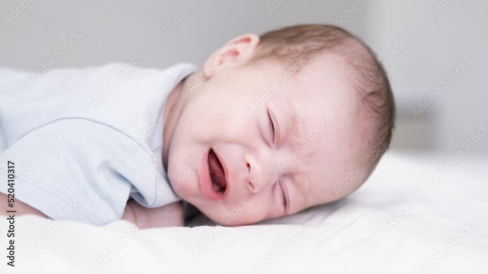 Dissatisfied, crying, upset, sad Newborn baby boy lying in nursery cocoon with blue clothes on bed in bedroom at home, baby morning Dissatisfied, crying, upset, sad Newborn baby boy lying in nursery cocoon with blue clothes on bed in bedroom at home, baby morning