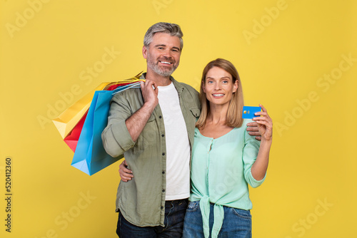 Wallpaper Mural Portrait of happy middle aged spouses holding shopping bags and credit card, smiling at camera over yellow background Torontodigital.ca