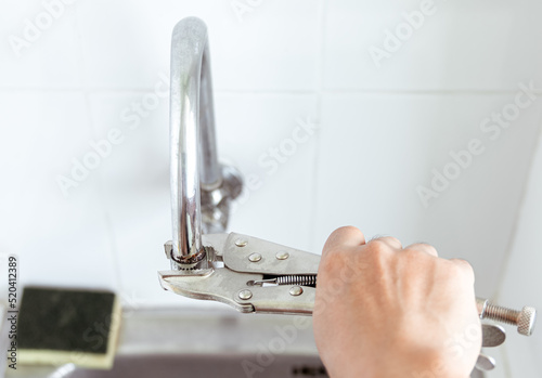 Close up view. Hand of person using lock pliers tong at the end of faucet. Old and rusty to screw out the tip.