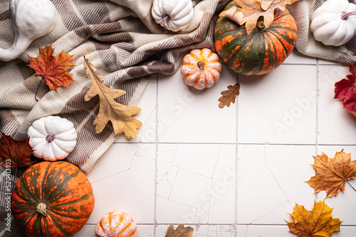 Cozy autumn flat lay with pumpkins, plaid and autumn leaves on tile background. Autumn home decor. Cozy fall mood. Thanksgiving. Halloween.