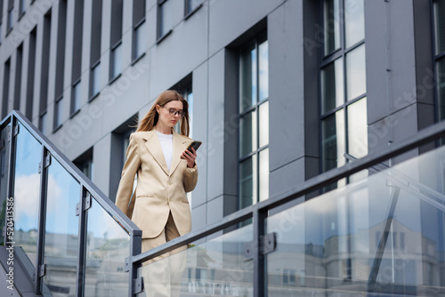 A young blonde girl against the backdrop of a business center, office center. On the go, he reads the news from his smartphone.