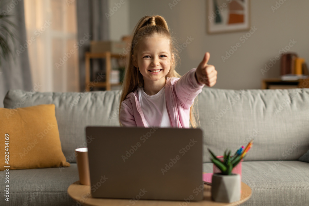 Schoolgirl Using Laptop Gesturing Thumbs Up Approving E-Learning At Home Schoolgirl Using Laptop Gesturing Thumbs Up Approving E-Learning At Home