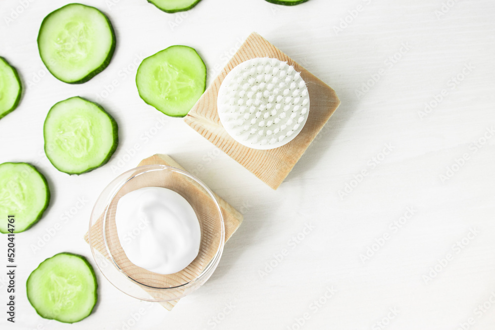 A sample of a moisturizing cosmetic product and a piece of green cucumber on a white wooden background with copy space. Body care, spa and beauty. A sample of a moisturizing cosmetic product and a piece of green cucumber on a white wooden background with copy space. Body care, spa and beauty.