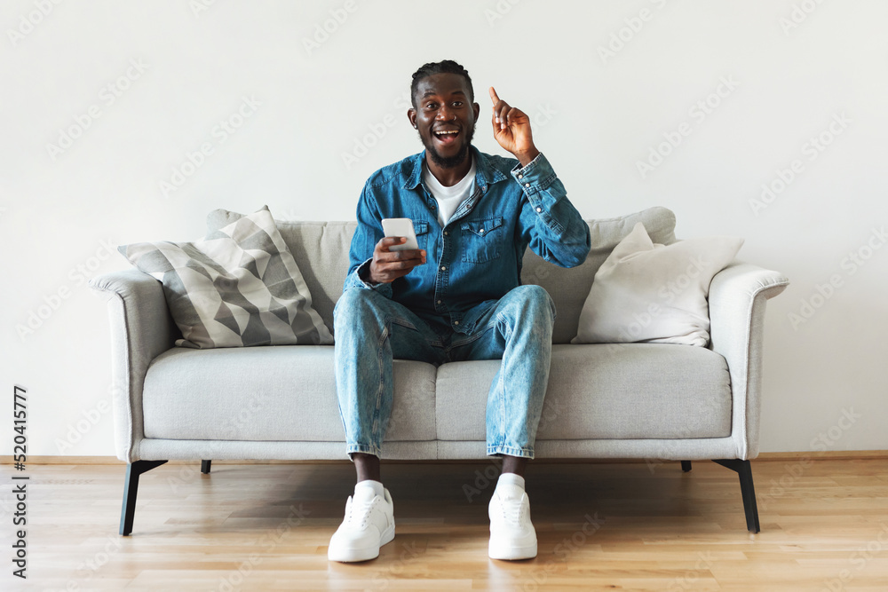 Excited African American Guy Holding Smartphone Having Idea Sitting Indoors