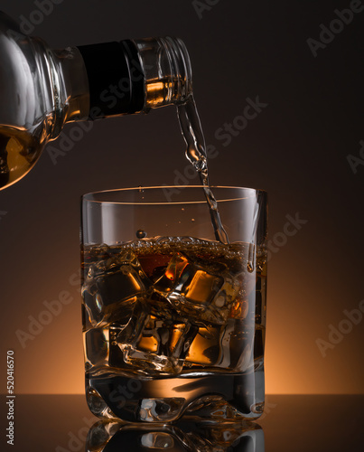 Obraz na plátně Glass of whisky with ice , a glass of whisky is poured from a bottle