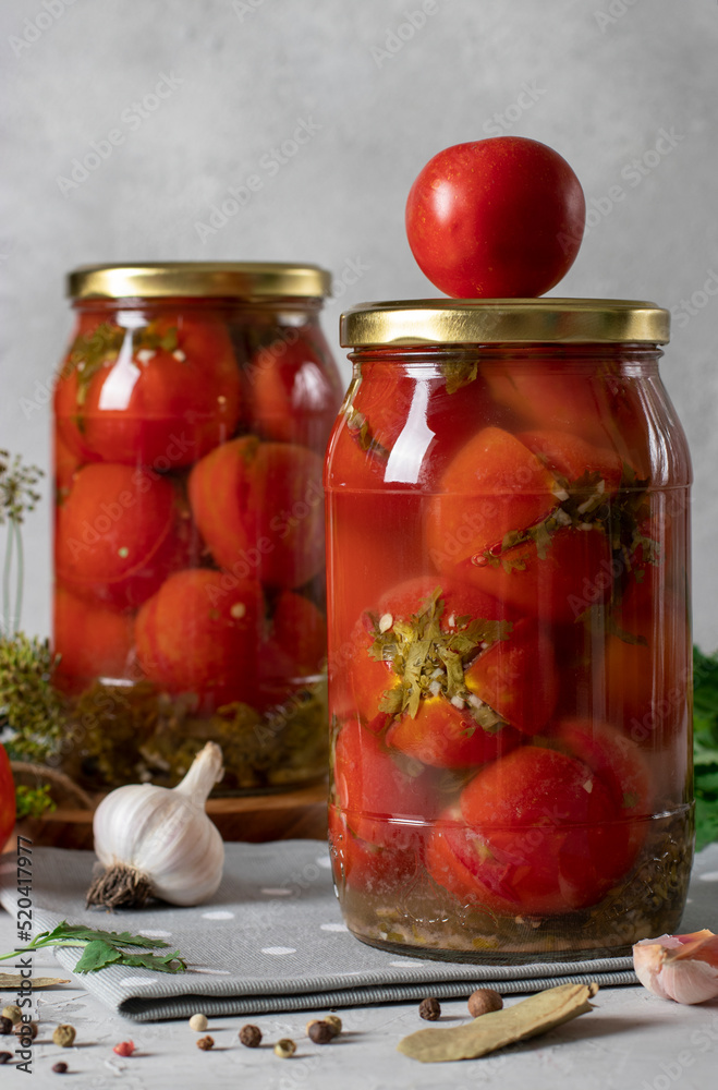 Marinated tomatoes with cilantro in jars for the winter on light gray background Marinated tomatoes with cilantro in jars for the winter on light gray background