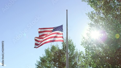 American flag dramatically waves at half mast with bright hopeful sun flaring photo