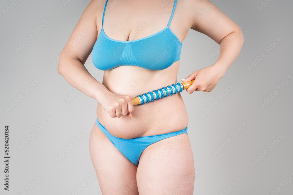 Fat woman with anti-cellulite roller massager on gray background