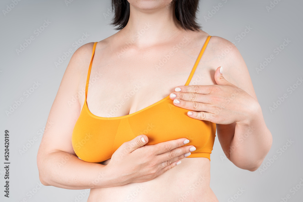 Breast test, woman in orange bra examining her breasts for cancer on gray  background Stock Photo