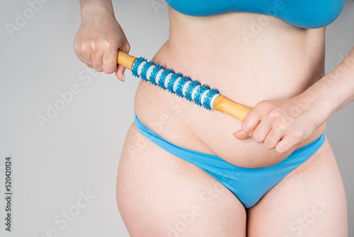 Woman with anti-cellulite roller massager on gray background photo