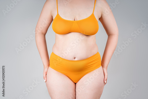 Fat woman in orange underwear on gray background, overweight female body