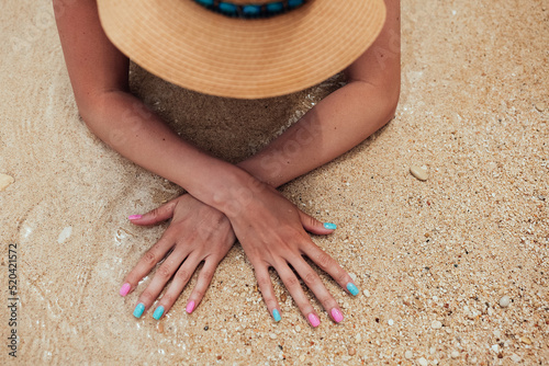 Sticker Beautiful female hands with pink and blue manicure nails on sea sand background
