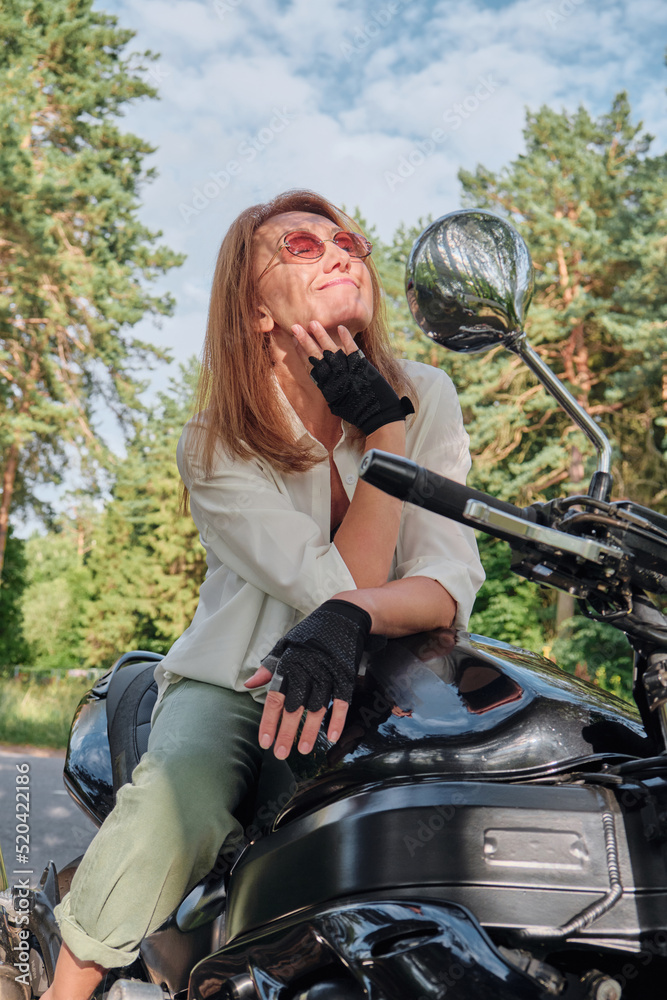 Middle age woman biker drives a motorcycle on a forest road, travels alone Middle age woman biker drives a motorcycle on a forest road, travels alone