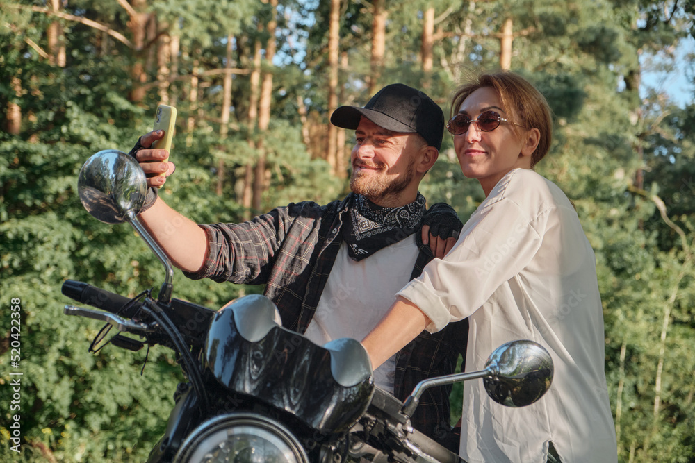 Middle age couple riding a motorcycle having fun and taking a selfie on a mobile phone camera