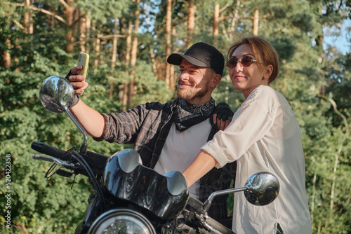 Middle age couple riding a motorcycle having fun and taking a selfie on a mobile phone camera