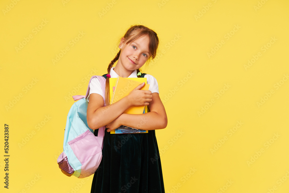 Portrait of a schoolgirl with textbooks and a backpack on a yellow background. Back to school Portrait of a schoolgirl with textbooks and a backpack on a yellow background. Back to school
