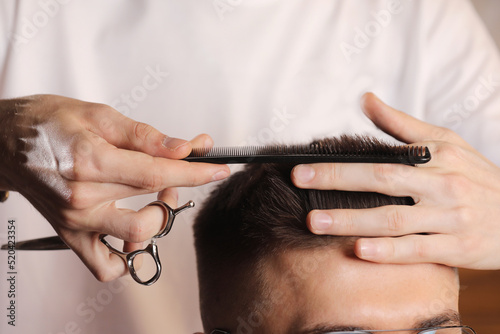 Hands of barber using scissors to cut customer's hair in salon. barber cuts hair, hairstyle. Male customer sitting in chair in hairdressing salon or barbershop. Creating new hair look.