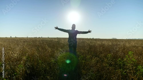 Farmer businessman with raised hands walks through the wheat field at sunrise. Man agriculturist silhouette at walk. Agriculture farming business concept. harvest