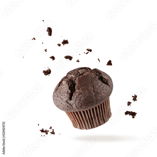Fresh baked single chocolate muffin with crumbs flying on white background. Sweet dark cupcake falling. photo
