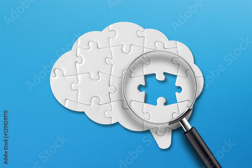 Brain shaped white jigsaw puzzle on blue background. Searching missing piece of the brain puzzle with magnifying glass. Mental health and problems with memory. 
