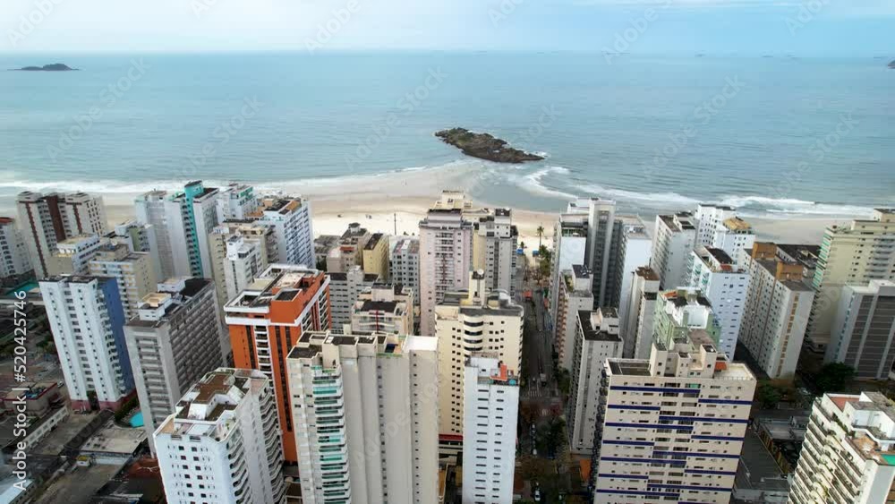 Praia das Asturias localizada na cidade do Guarujá, interior de São Paulo.  Dia nublado com pessoas caminhando pela praia. 