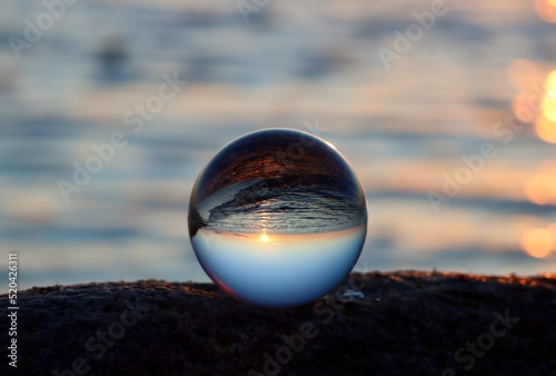 Fotografie Crystal ball on rocky beach on a granite boulder, sunset reflecting in the sea,