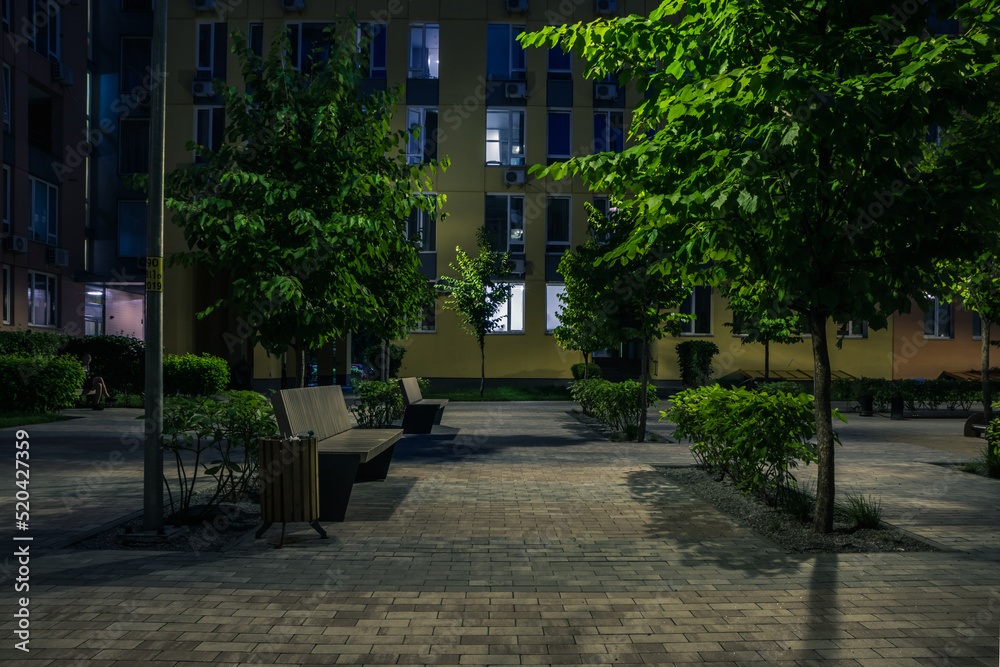 Obraz premium Night park paths and colored houses at summer night. Night paths, benches and lanterns in a beautiful residential complex. Night summer park with lanterns and benches. Kyiv. Ukraine