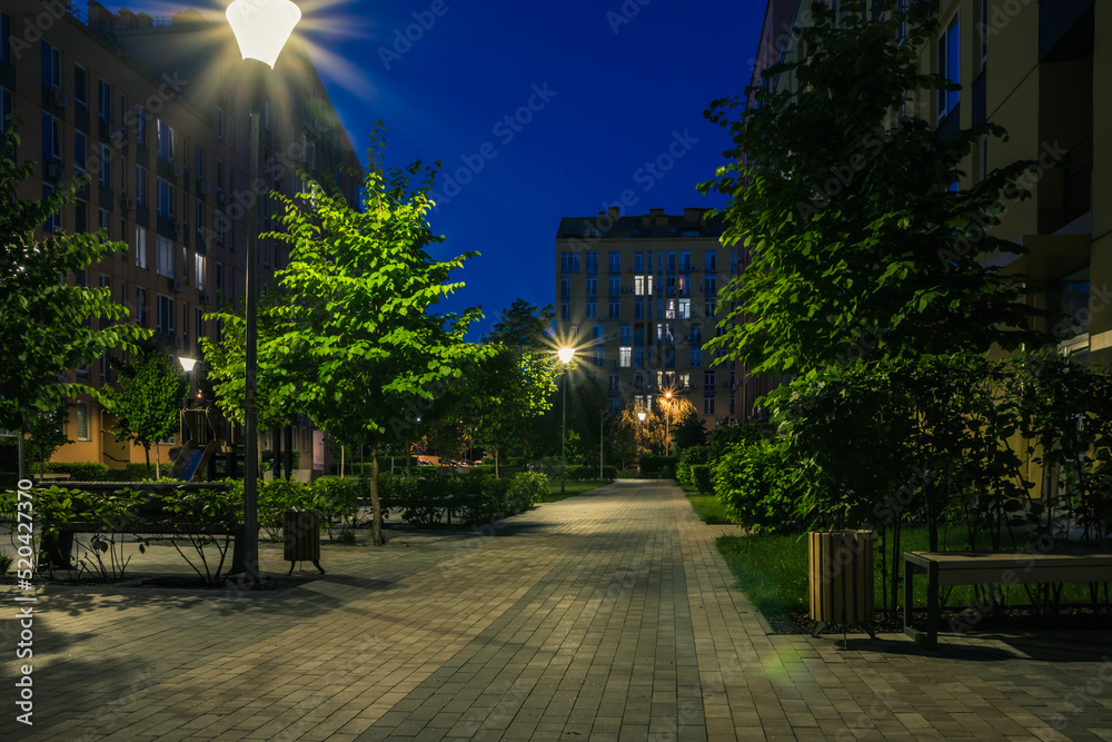 Night park paths and colored houses at summer night. Night paths, benches and lanterns in a beautiful residential complex. Night summer park with lanterns and benches. Kyiv. Ukraine Night park paths and colored houses at summer night. Night paths, benches and lanterns in a beautiful residential complex. Night summer park with lanterns and benches. Kyiv. Ukraine