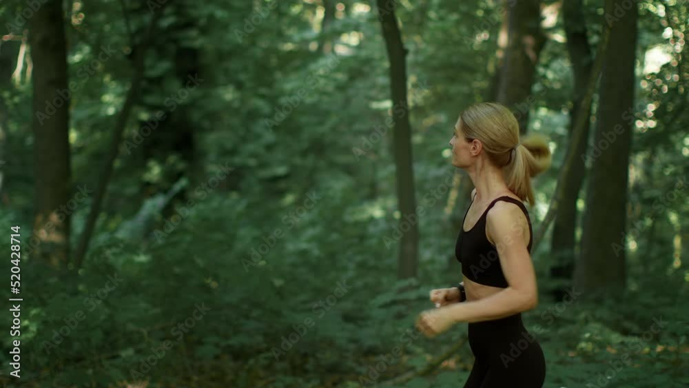Active cardio training. Side view of of sporty woman running in woodland, enjoying nature during workout, follow shot Active cardio training. Side view of of sporty woman running in woodland, enjoying nature during workout, follow shot
