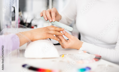 Fotografia Young woman hands in a nail salon, which the manicure master files the nails wit
